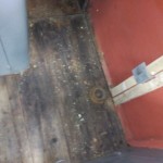 Původní dřevěná podlaha. V pravé části odkrytý bok stanoviště, kde byla odstraněna stará tepelná izolace a kov obroušen a natřen základní barvou.